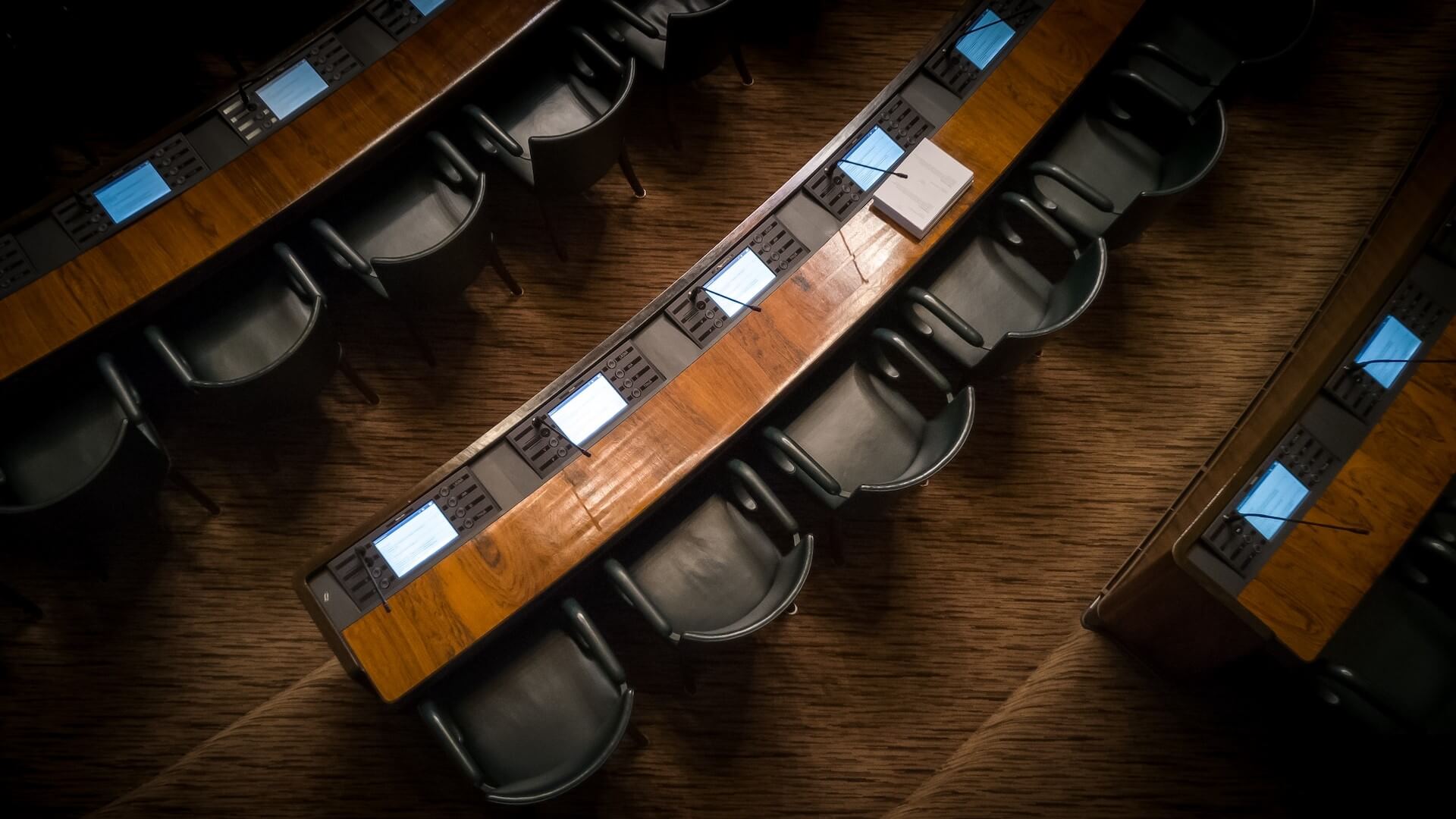 Disposição dos lugares numa sala do Parlamento, equipada com microfones e ecrãs para debates e apresentações.